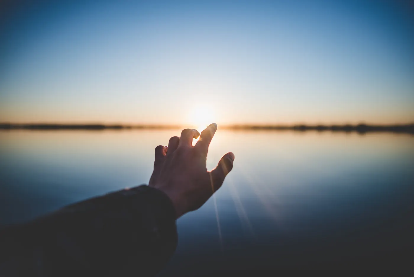 hand reaching out into the sunset on the backdrop of an ocean